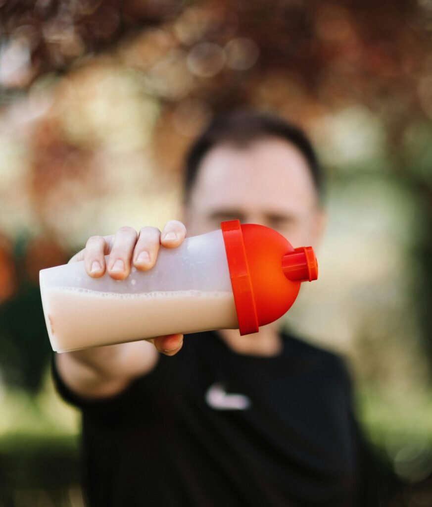 pexels-photo-4378601-4378601-1 Focus on a man holding a plastic protein shake tumbler outdoors with a blurred background.
