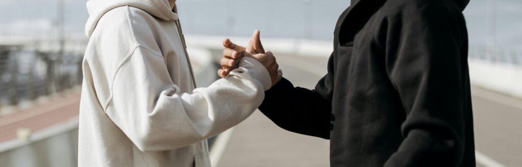 Two people in hoodies shake hands outdoors, symbolizing friendship and connection.