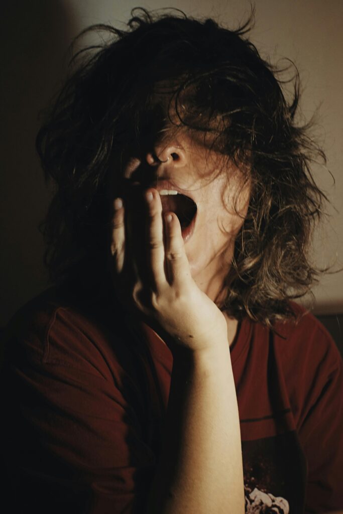 pexels-photo-3416980-3416980 A woman with bed hair yawns in dim lighting, depicting fatigue and morning mood.