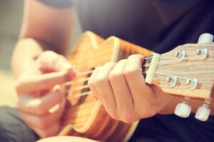 A person strums a wooden ukulele outdoors, enjoying leisure and music in the sun.