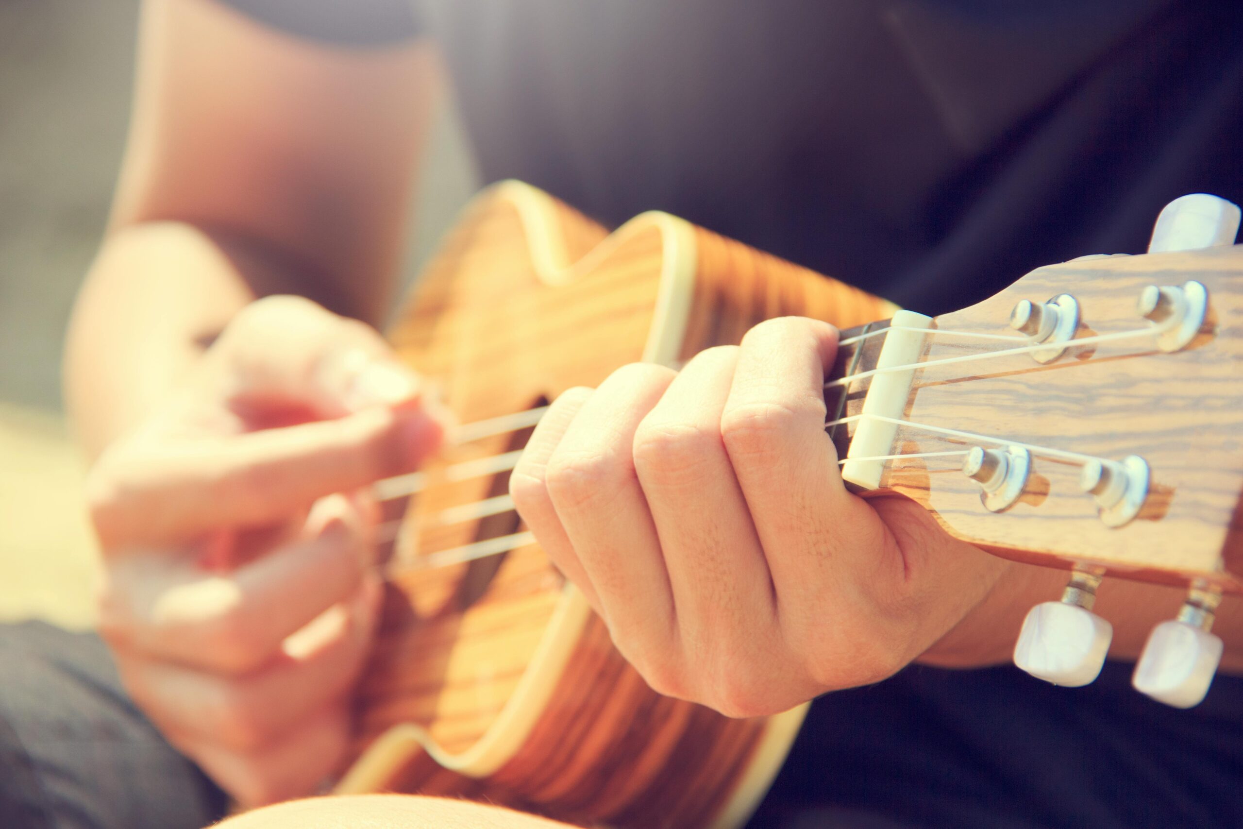 A person strums a wooden ukulele outdoors, enjoying leisure and music in the sun.