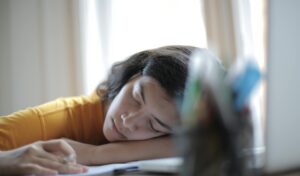 Young woman in yellow shirt resting her head on a desk, showing signs of fatigue and relaxation indoors.