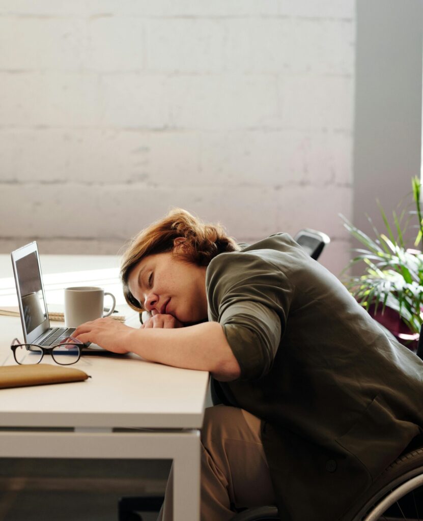 pexels-photo-4064169-4064169 A tired woman in a wheelchair sleeps at her desk in a modern office setting.