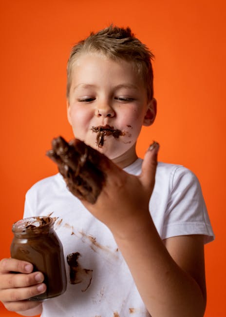 pexels-photo-4720368-4720368 A happy child with messy hands indulges in chocolate against an orange background.