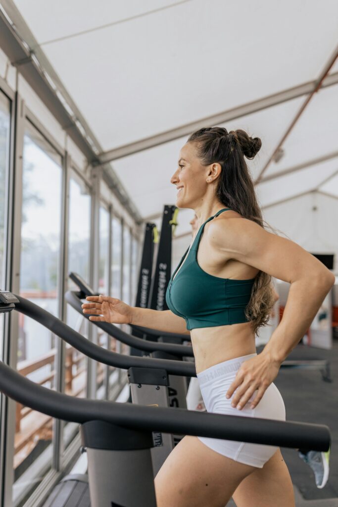 pexels-photo-4944975-4944975 Fit woman jogging on treadmill in an airy gym, focused on health and fitness.