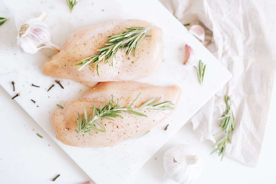 pexels-photo-5769375-5769375 Raw chicken breasts seasoned with rosemary and garlic on a cutting board.